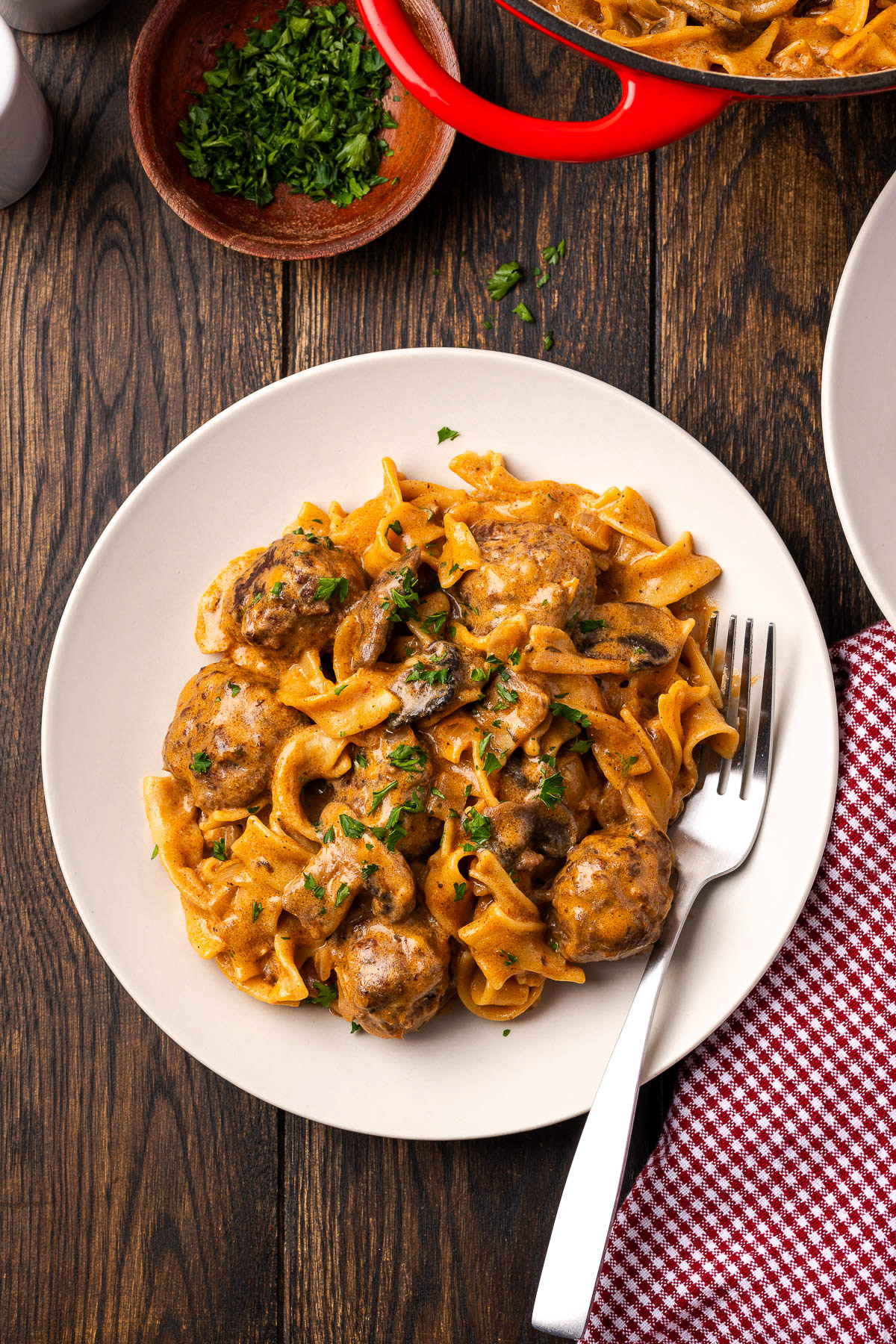 Plated meatball stroganoff with a fork, the cast iron Dutch oven and parsley in the background