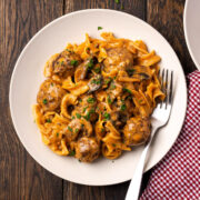 Plate of meatball stroganoff with egg noodles, mushrooms and parsley on a wooden table