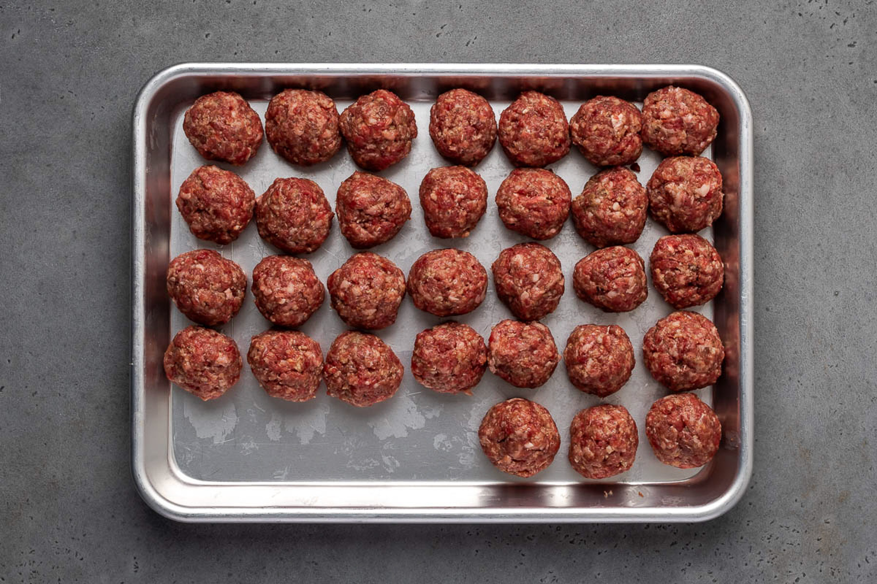 Raw homemade beef meatballs rolled and lined up on a sheet pan