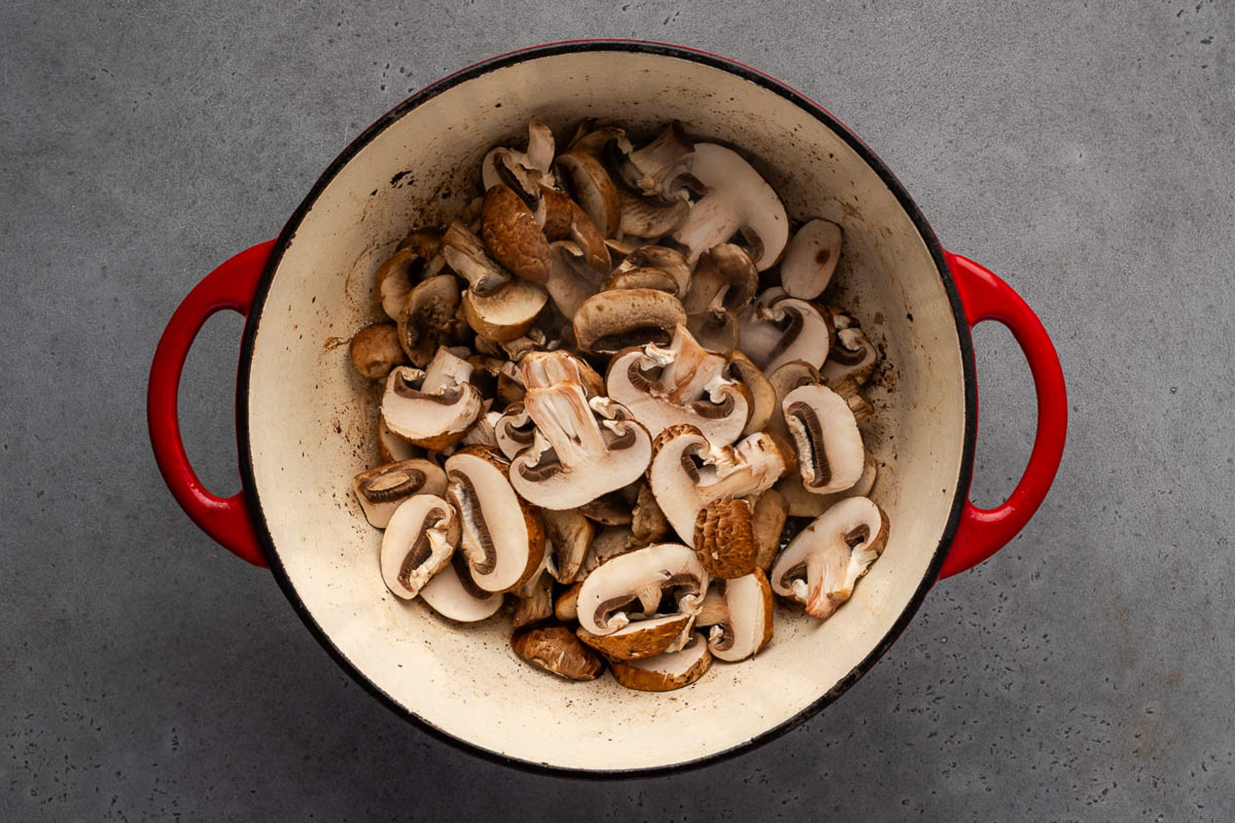 Sliced cremini mushrooms in a cast iron Dutch oven ready to brown