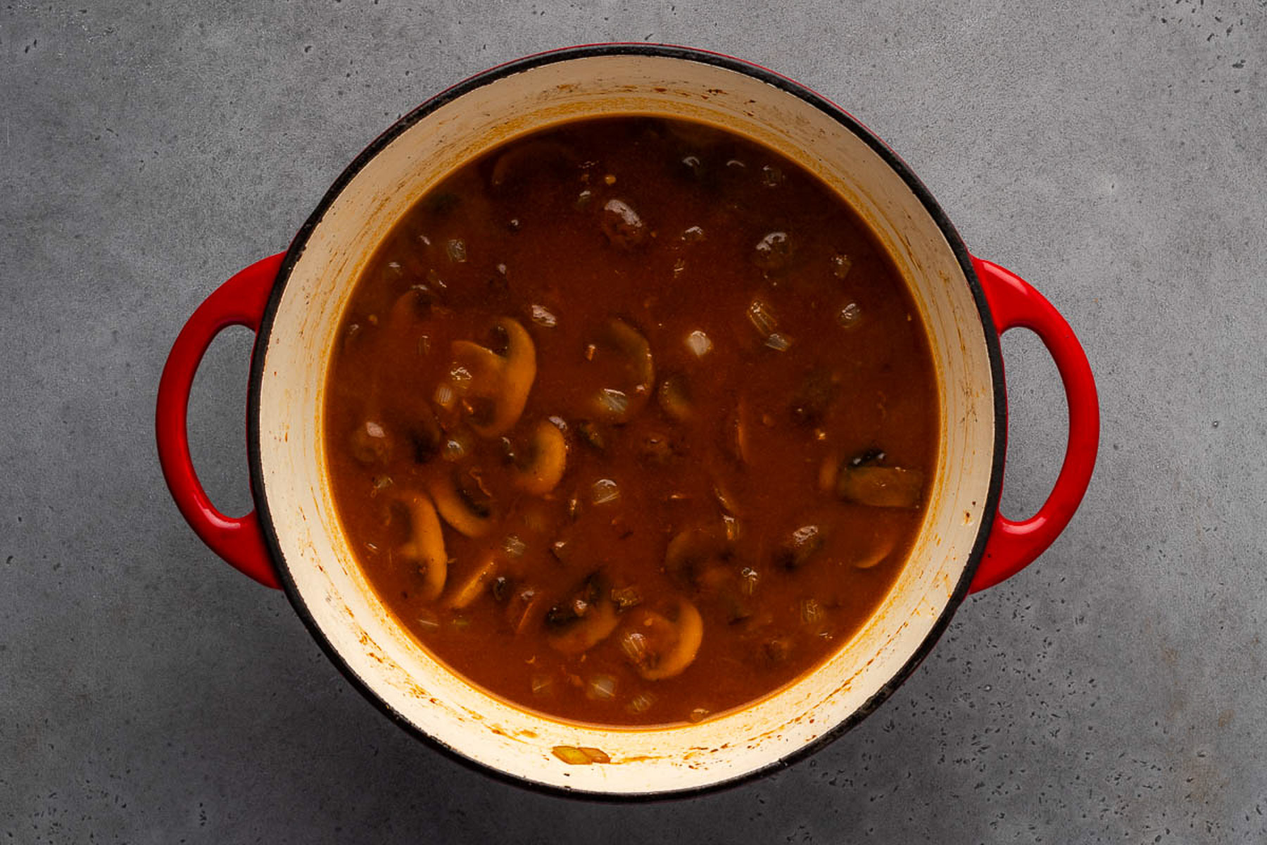 Beef broth and mushrooms simmering into a stroganoff sauce in a Dutch oven