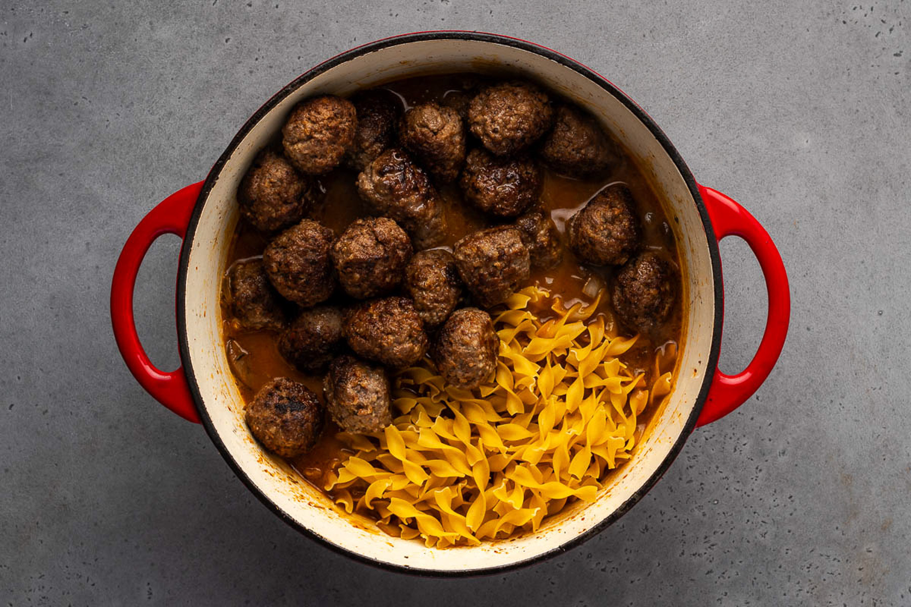 Browned meatballs and dry egg noodles added to the stroganoff sauce in a Dutch oven