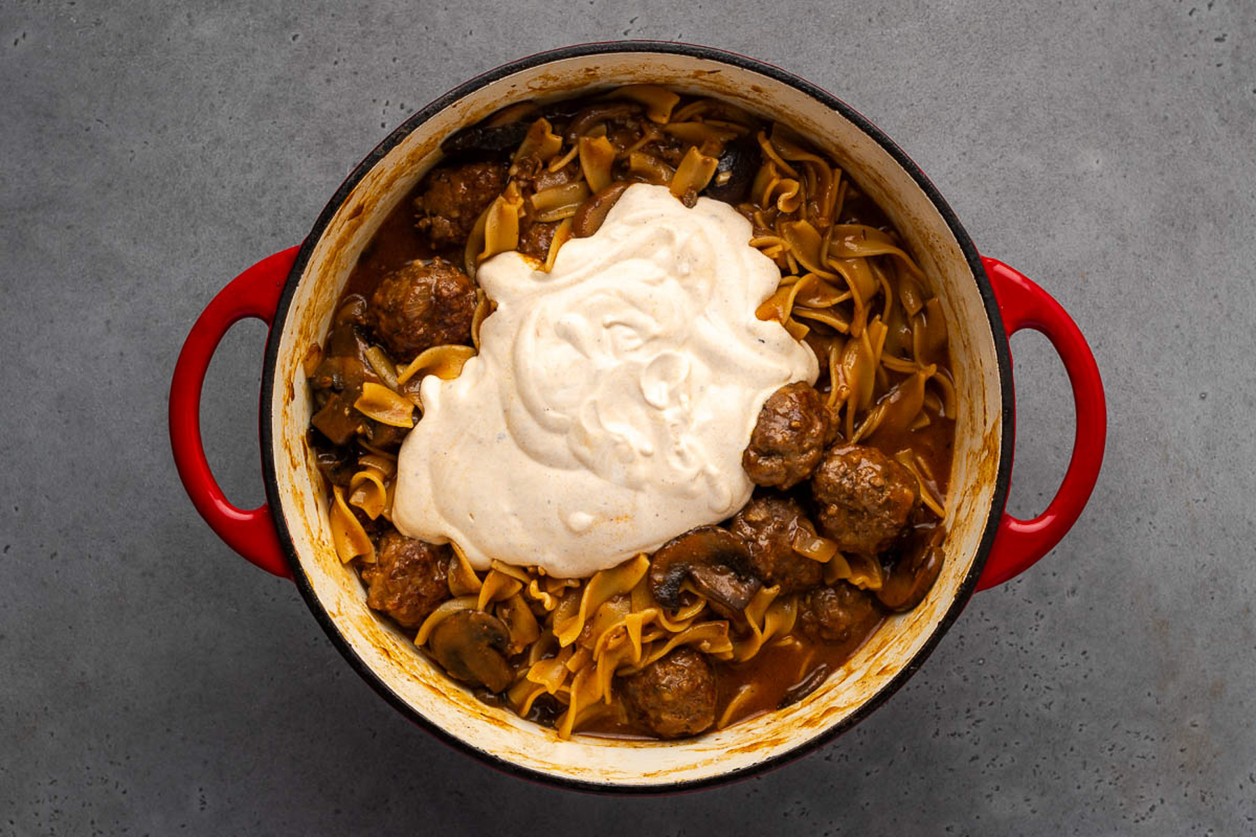 Tempered sour cream added on top of meatballs and noodles in a cast iron Dutch oven