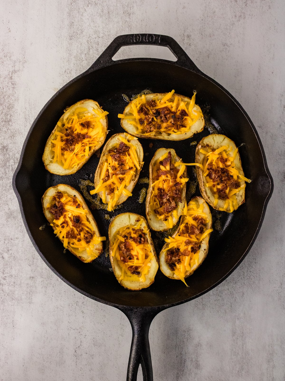 Potato skins filled with shredded cheddar and bacon in a cast iron skillet before melting
