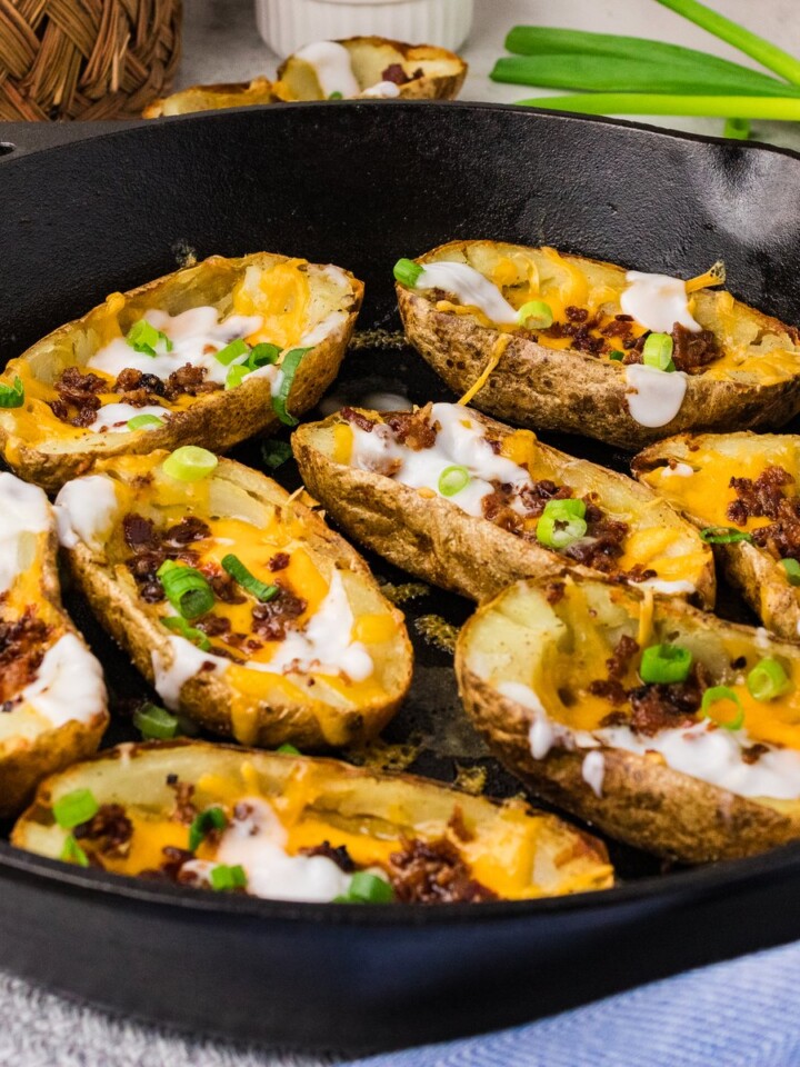Potato skins in a cast iron skillet topped with cheddar, bacon, sour cream and green onions